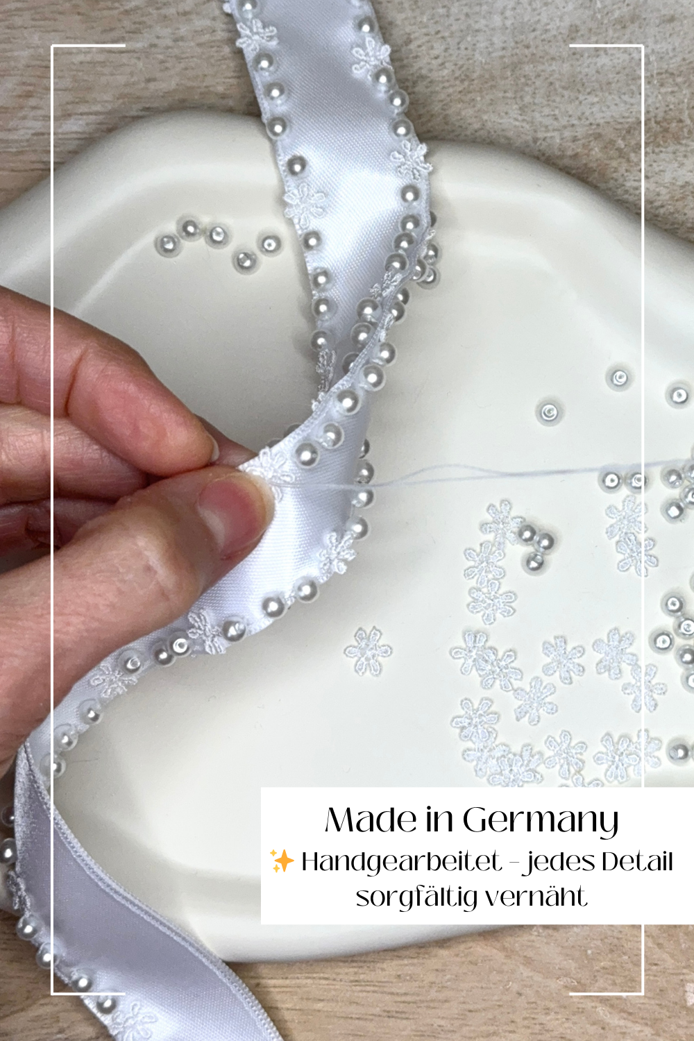 Nahaufnahme zweier Hände, die Perlen mit einer Nadel auf ein weißes Stoffband nähen.