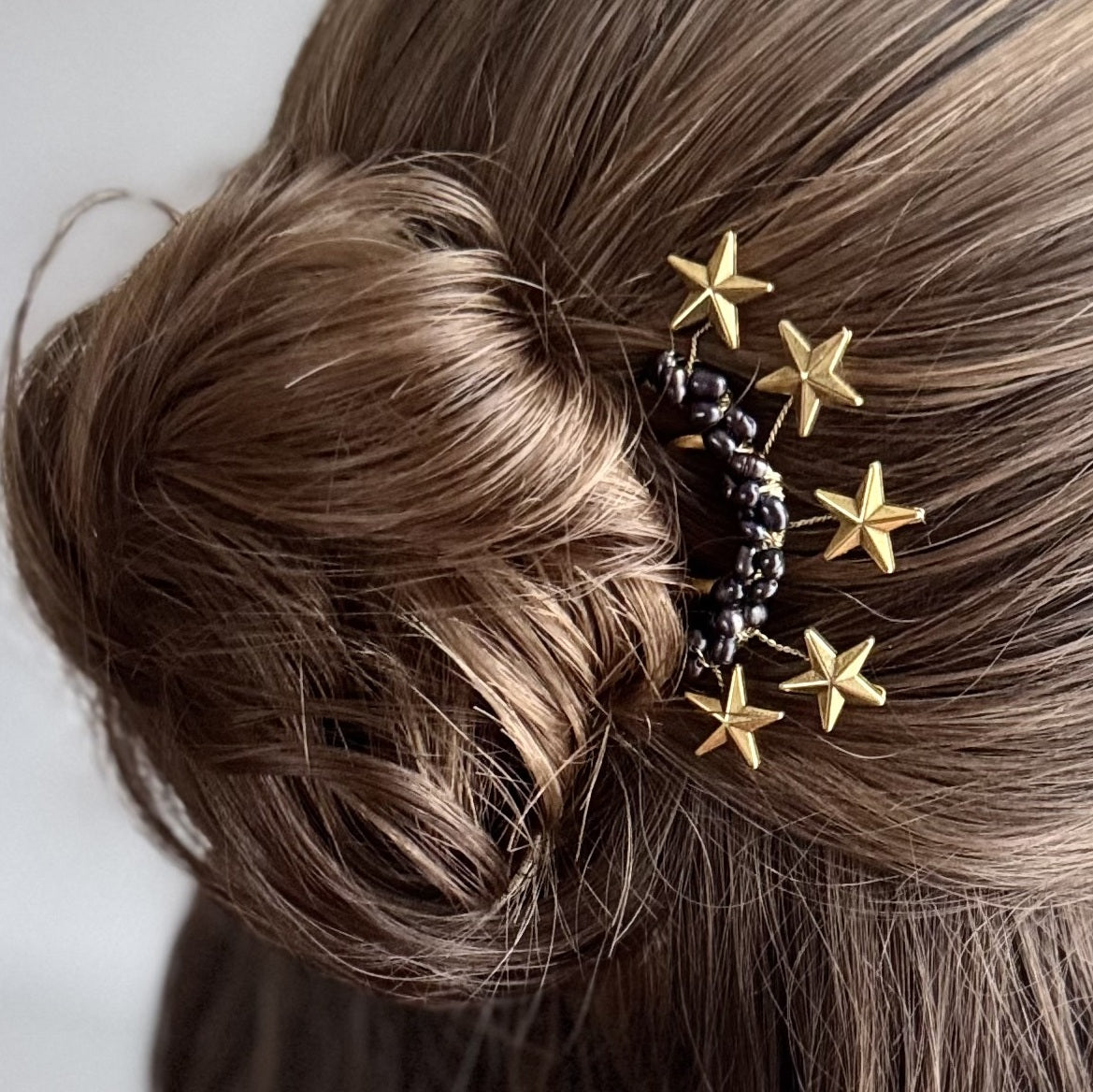 Goldener Sternen-Haarschmuck in einem eleganten Dutt, goldene Sterne und dunkle Perlen detailreich im Haar platziert.