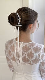 Mädchen mit festlicher Duttfrisur, verziert mit weißem Haarschmuck aus Perlen und Blumen zur Kommunion