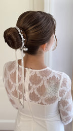 Mädchen im weißen Kleid mit festlicher Duttfrisur, dekoriert mit Blumen-Perlen-Haarschmuck für die Erstkommunion.