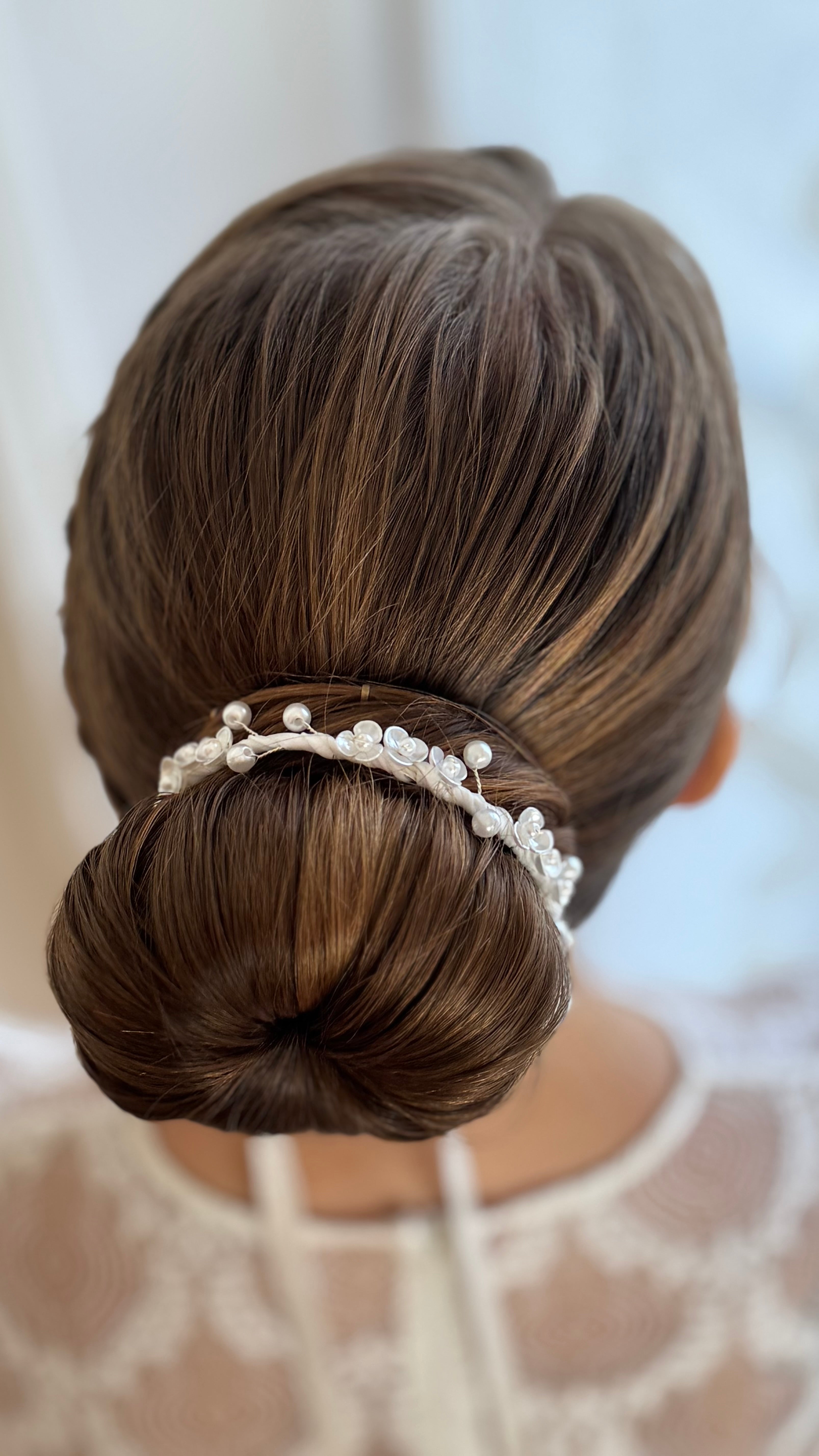 Weißes Duttband mit Perlen und Blumen, eng um eine elegante Kommunionsfrisur gebunden, festlicher Look für Mädchen.