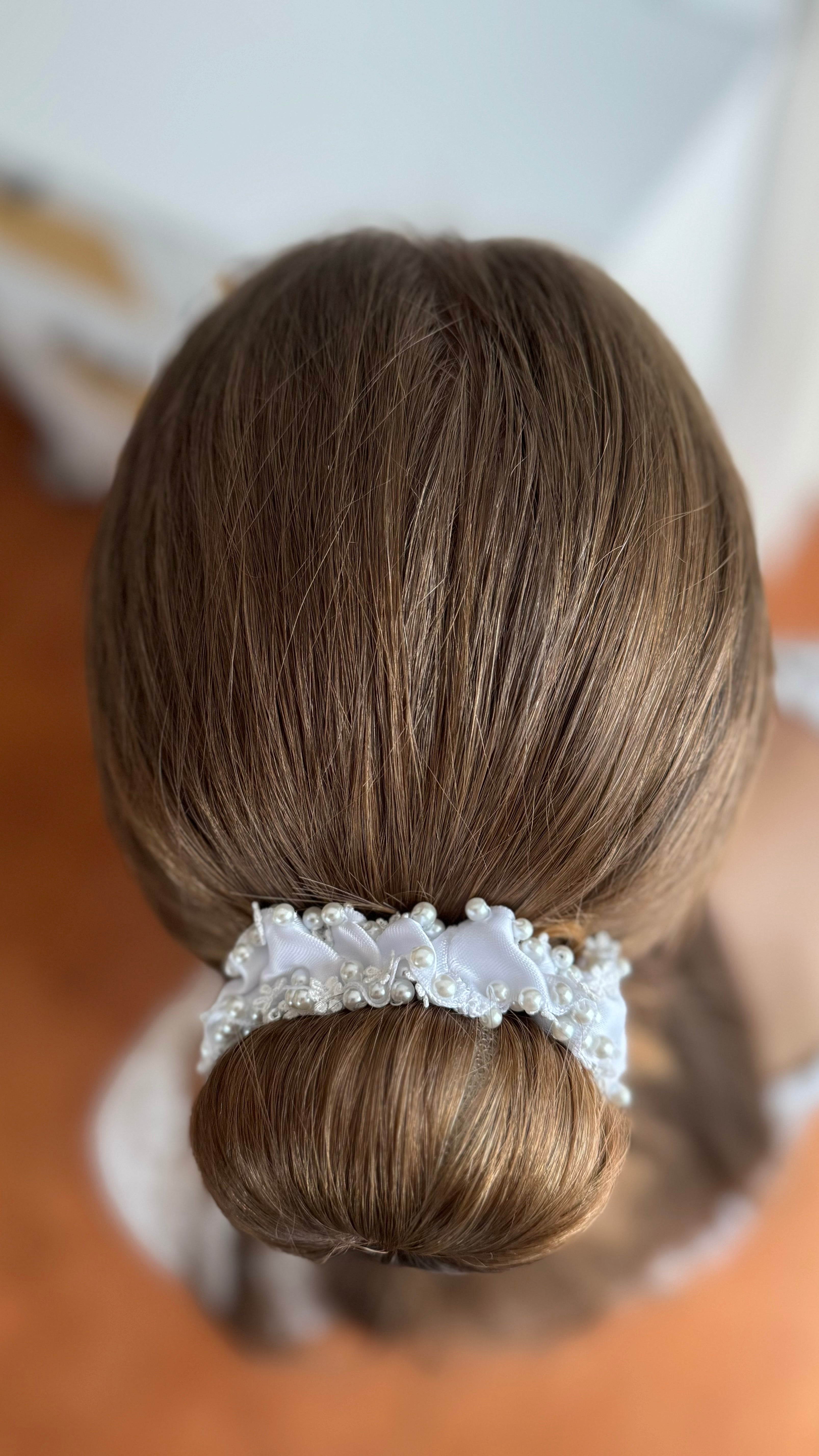 Ansicht von oben auf denselben Dutt mit dem weißen, perlenbesetzten Haarschmuck, der sich gleichmäßig um den Knoten legt.