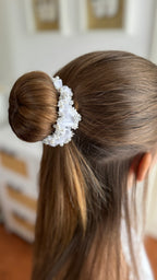 Seitliche Ansicht eines Dutts, der von einem weißen Haarschmuck mit Perlen und Spitzenapplikationen umschlossen ist.