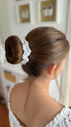 Rückansicht einer hochgesteckten Frisur mit einem glatten Dutt, der von einem weißen Haarschmuck mit Perlenverzierung umgeben ist.