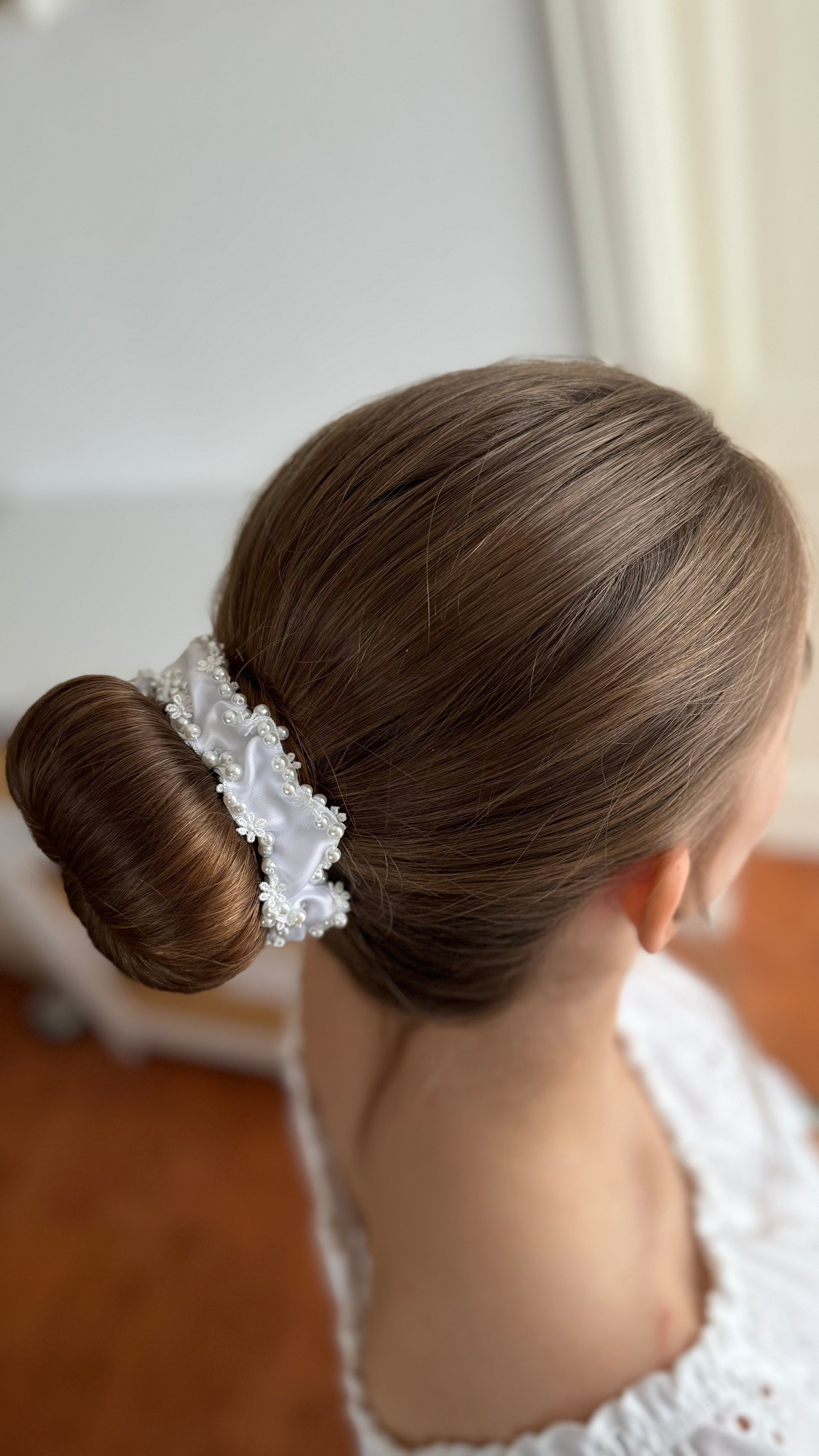 Seitliche Draufsicht auf einen tiefen Dutt, eingefasst von einem weißen Haarschmuck aus Stoff, Spitze und Perlen.