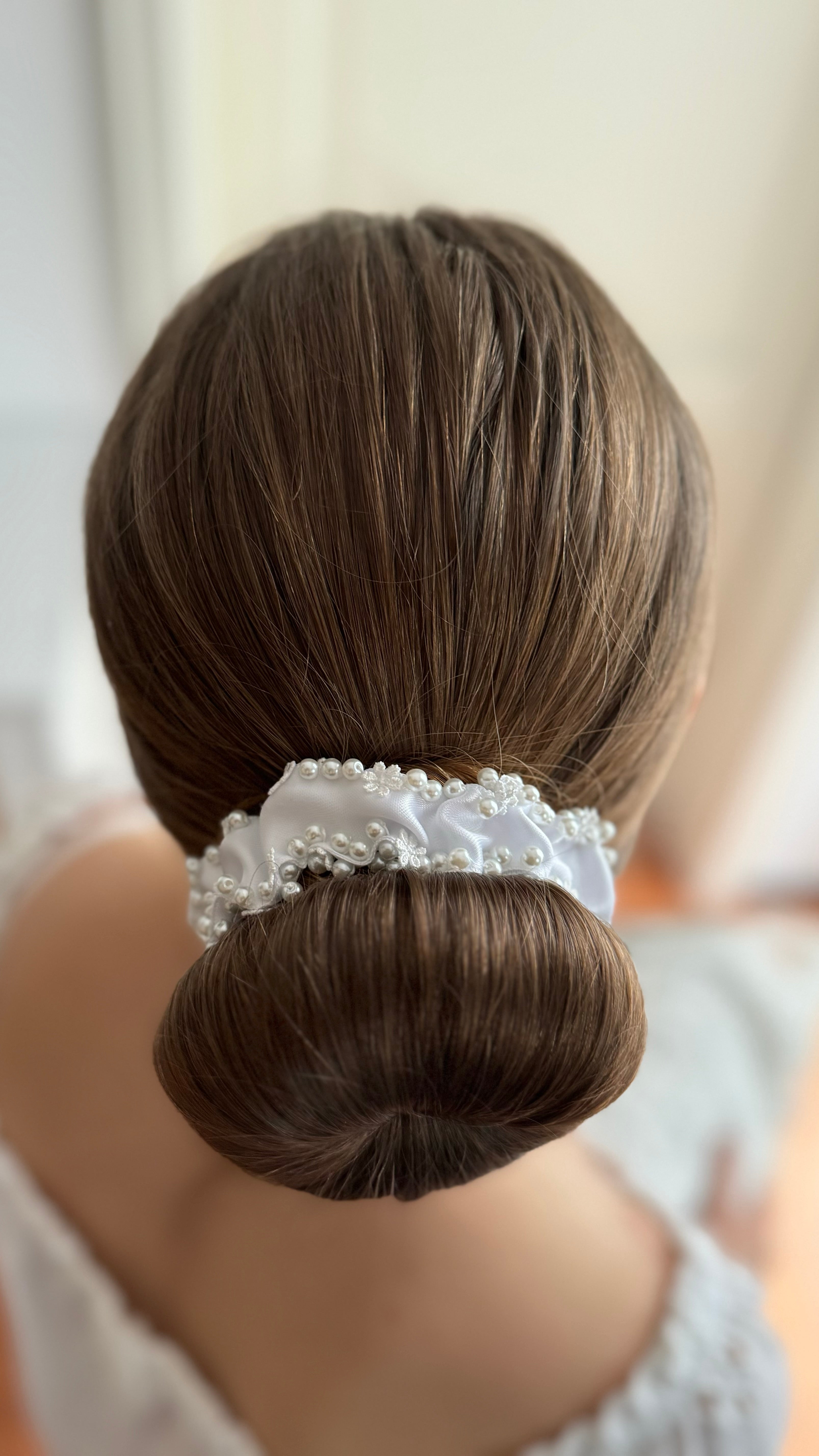 Rückansicht eines Dutts, umschlossen von einem weißen Haarschmuck mit perlenbesetzten Spitzenblüten.