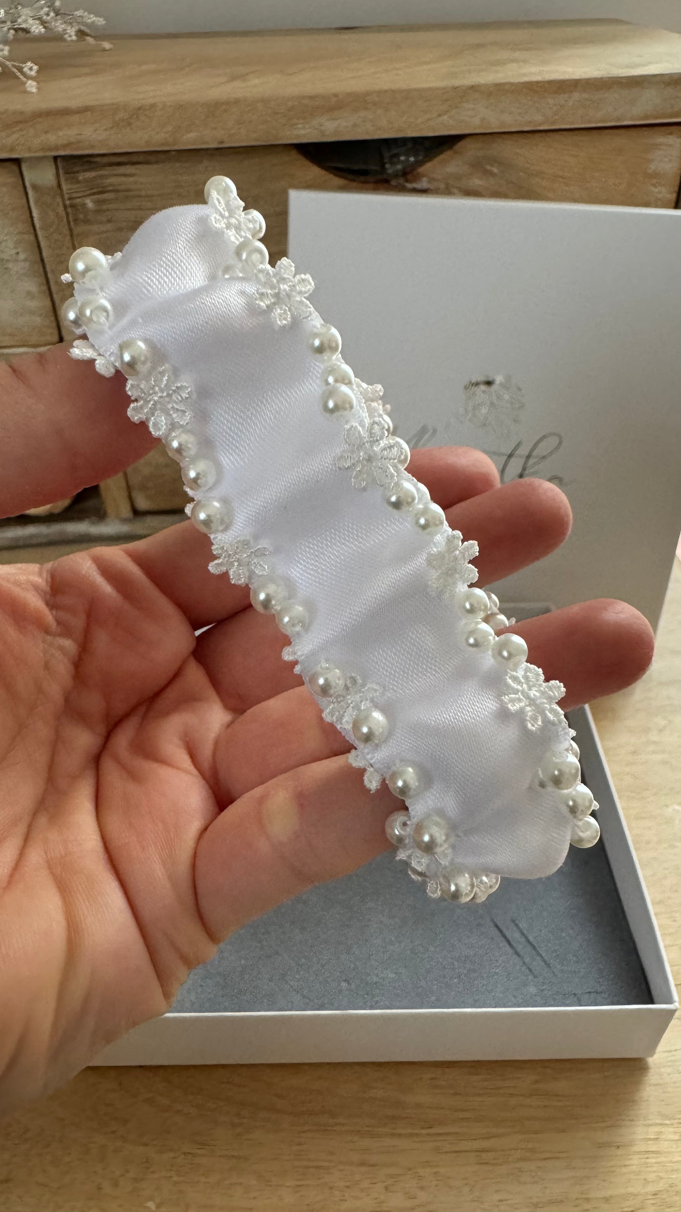 Nahaufnahme einer Hand, die den weißen Haarschmuck mit Perlen und Spitzenapplikationen hält.